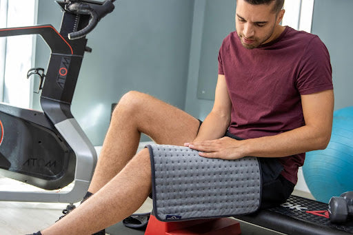 A person in a gym using an electric heat pad to alleviate discomfort to their upper leg